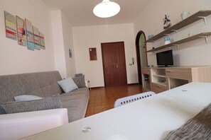 Ein Wohnzimmer mit einer Couch, einem Fernseher auf einem Schrank, einer Tür und einer Wand mit abstrakter Kunst.
