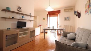 Ein Wohnzimmer mit Fernseher, Holzmöbeln, einem Esstisch und einer Couch.