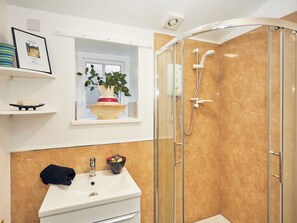 Een badkamer met douche, wastafel, raam met plant en een fotokader aan de muur.
