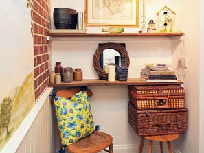 A corner room with a wooden shelf, wicker baskets, a chair with a floral cushion, and a framed map on the wall. - Apple Bough Cottage (Hereford)