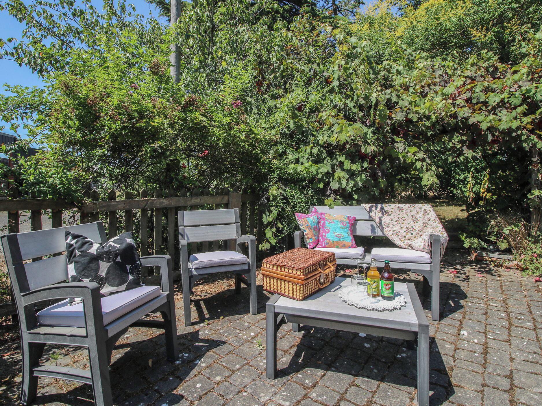 An outdoor seating area with two chairs and a table, a wicker basket, and a bottle of drink.
