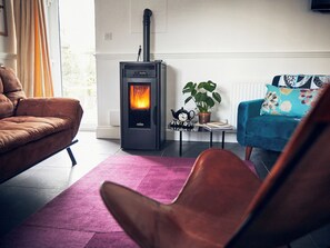 A living room with a fireplace, a sofa, a chair, a table with a plant and a teapot, and a radiator. - Apple Bough Cottage (Hereford)