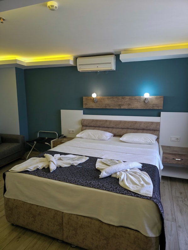 A hotel room with a bed, bedside tables, a wall-mounted air conditioner, and a ceiling light fixture.