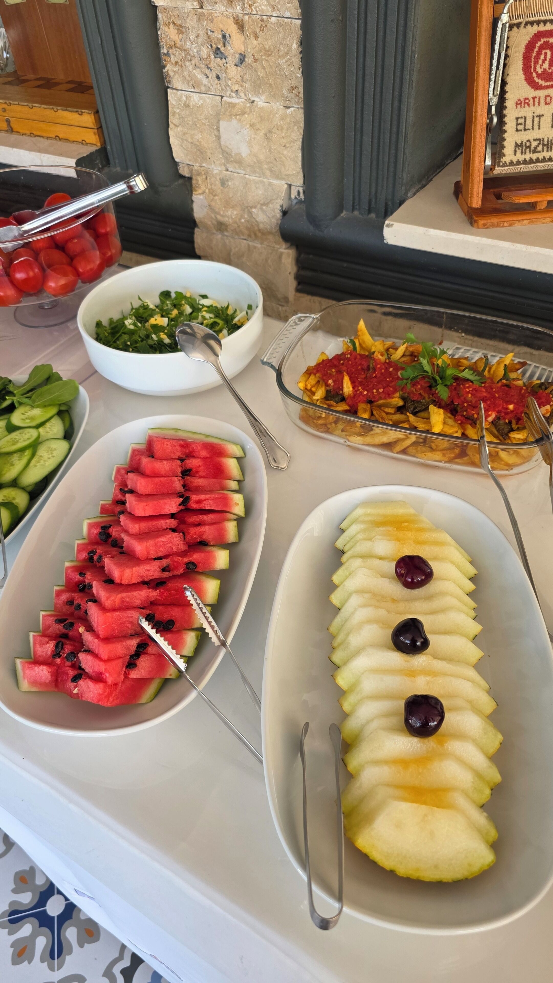 Een buffet met diverse gerechten, waaronder watermeloen, appels en een salade.