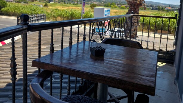 Una mesa de madera con baranda metálica, una palmera y vista a un paisaje rural.