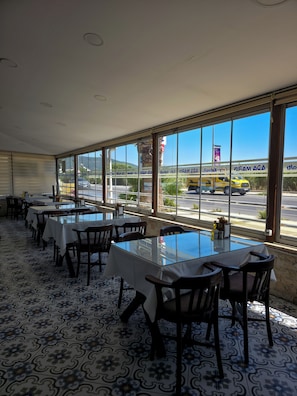 A restaurant with tables and chairs, large windows, and a view of the street outside. - Ada Marin Hotel (Urla)