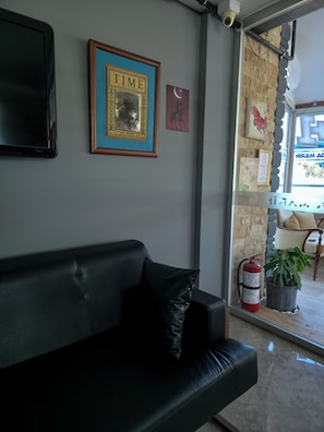 A black leather sofa with a cushion, a framed TIME magazine, a small framed picture, a fire extinguisher, and a potted plant. - Ada Marin Hotel (Urla)