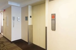 A hotel hallway with a phone, a wall-mounted intercom, and an elevator with a safety sign.