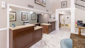 A reception area with a marble floor, wooden reception desk, framed pictures on the wall, and a staircase leading to another level. - Pet-Friendly Room | Free Breakfast (Williamsburg)