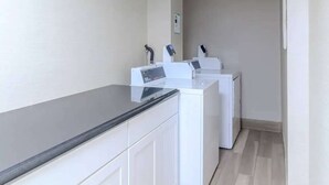 A laundry area with a washing machine and dryer, a countertop, and a wall-mounted control panel. - Pet-Friendly Room | Free Breakfast (Williamsburg)