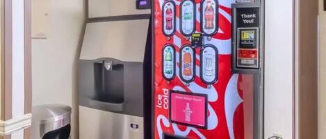 A Coca-Cola branded vending machine with a digital payment screen and a trash bin nearby.