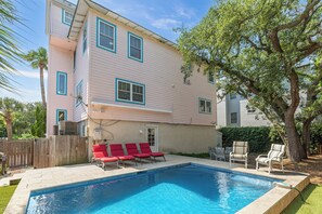 A two-story house with a swimming pool, red lounge chairs, and a wooden fence. - Private Heated Pool, Rooftop Views & Steps to Best Beaches by Tybee Cottages (Tybee Island)