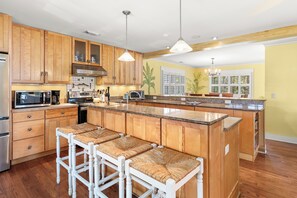 A kitchen with wooden cabinets, a central island with bar stools, stainless steel appliances, and a large window. - Private Heated Pool, Rooftop Views & Steps to Best Beaches by Tybee Cottages (Tybee Island)