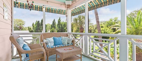 Eine überdachte Veranda mit Korbmöbeln, einem Deckenventilator und Blick ins Grüne.