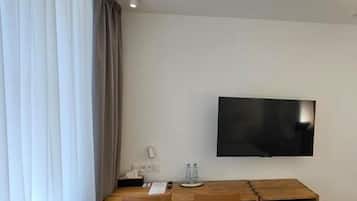 A hotel room with a desk, chairs, a flat-screen TV, and a large window with curtains.