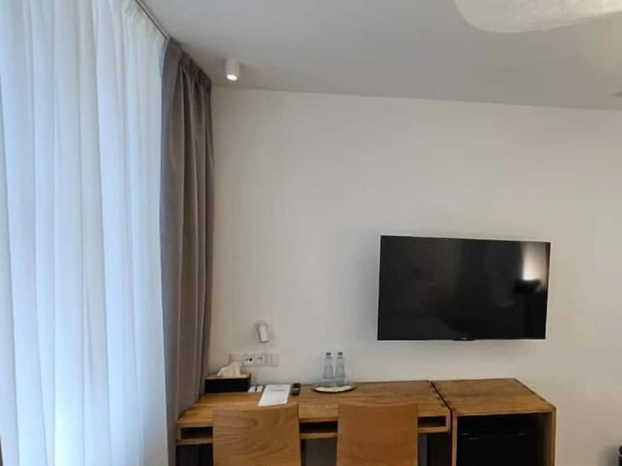 Ett hotellrum med ett skrivbord, stolar, en platt-TV och ett stort fönster med gardiner.