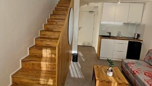 En trappe fører op til et alkovekøkken med et spisebord og en sofa i forgrunden.