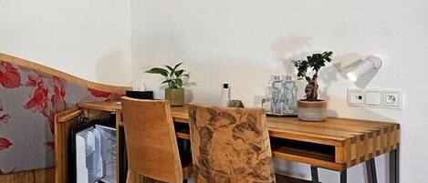 A small, neatly arranged workspace with a wooden desk, two chairs, and a wall-mounted lamp.