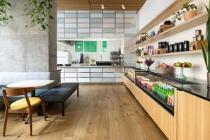 A modern cafe with wooden flooring, a counter with a menu, shelves with snacks, and a seating area with a table and chairs. - Steps to Union Square + Rooftop Bar & Gym (San Francisco)