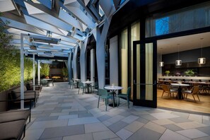 A modern outdoor dining area with tables and chairs, a fire feature, and a view into the interior dining space. - Steps to Union Square + Rooftop Bar & Gym (San Francisco)