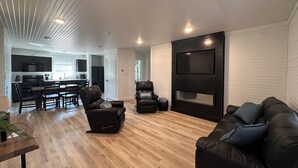 A modern living room with a fireplace, leather sofas, a dining area, and a kitchen in the background.