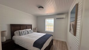 A bedroom with a bed, bedside lamps, a window, and an air conditioning unit.