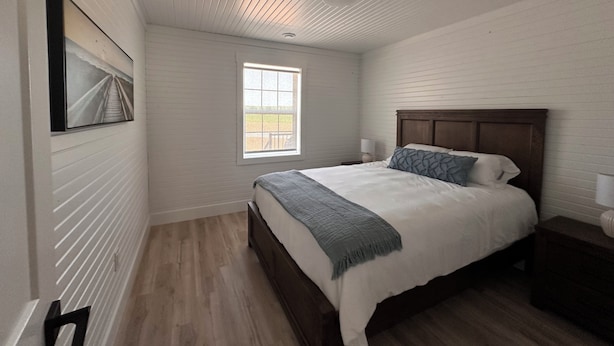 A bedroom with a bed, a nightstand, a window, and a picture on the wall.
