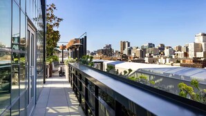 Une terrasse extérieure moderne offrant une vue sur la ville, avec des rampes en métal et de la verdure.