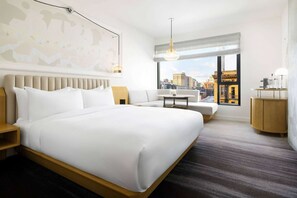 Habitació d'hotel amb un llit gran, una taula petita, un sofà, un escriptori i vistes a la ciutat.