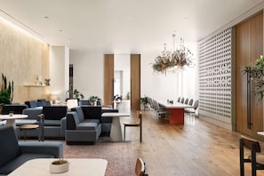 Una moderna hall d'albergo con aree salotto, una reception e un lampadario decorativo.