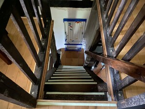 A wooden staircase with a handrail, leading to a room with a white wall and a blue object on the floor. - The Enchanted Cottage (Saint-Christophe-sur-Condé)
