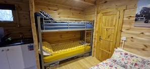Uma cama beliche com uma cama inferior, uma porta de madeira, um pequeno kitchenette e uma janela.
