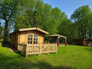 Una cabaña de madera con un área cercada, una mesa de picnic y un pabellón en un parque.