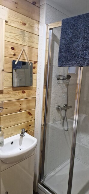 A bathroom with a wooden wall, a glass shower enclosure, a white sink, and a hanging mirror. - Bluebell Lodge Dog Friendly, nr Anderby Creek (Alford)