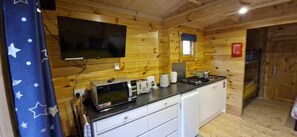 A compact kitchen with wooden walls, a flat-screen TV, a microwave, a toaster, and a small refrigerator. - Bluebell Lodge Dog Friendly, nr Anderby Creek (Alford)