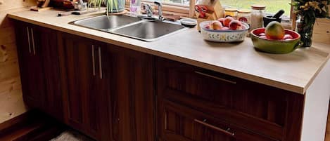 A wooden cabin kitchen with a large window, wooden cabinets, a sink, and various kitchen items.