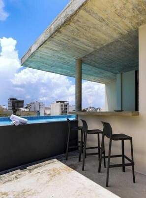 Eine Dachterrasse mit Beton Decke, einem Pool und zwei schwarzen Barhocker.