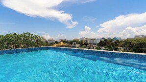 A clear blue swimming pool with a tiled edge, surrounded by greenery and buildings in the background. - Ocean Boutique Condos (Playa del Carmen)