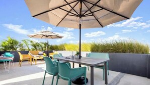 An outdoor patio with a table and chairs, two umbrellas, and a view of the sky and vegetation. - Ocean Boutique Condos (Playa del Carmen)