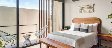 A modern bedroom with a large sliding glass door leading to a balcony, a wooden bed with a headboard, a bench, and a small side table with a plant.