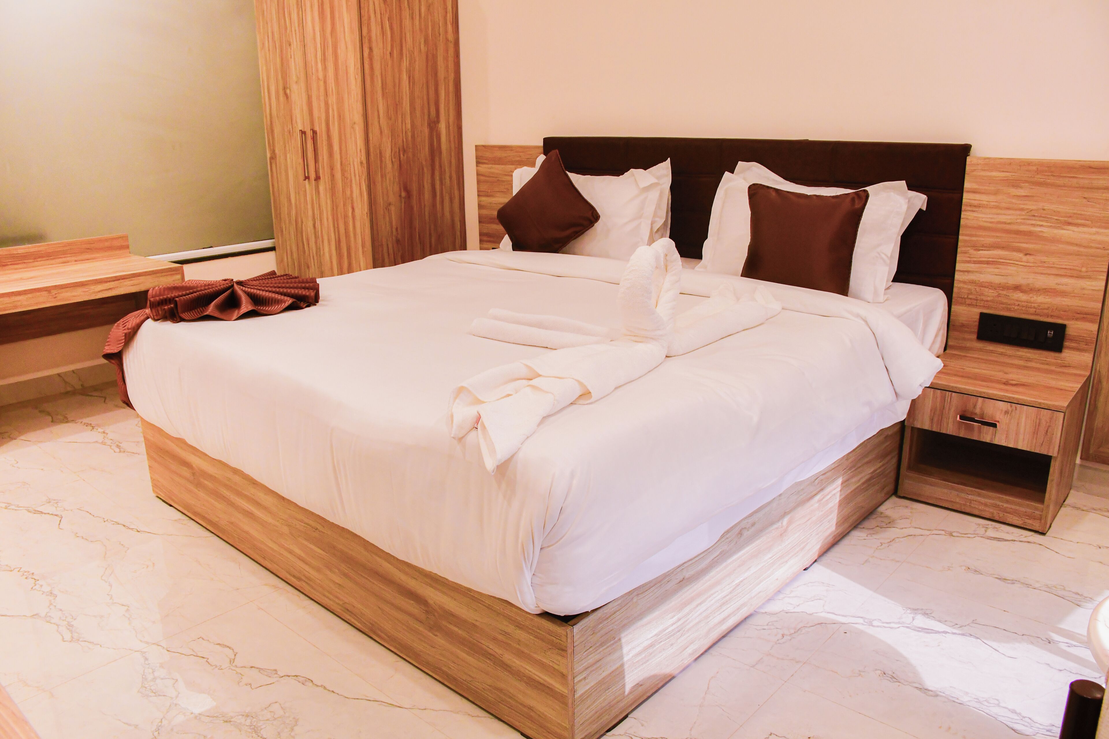 Habitación de hotel con una cama grande, cabecero de madera, ropa de cama blanca y piso de mármol.