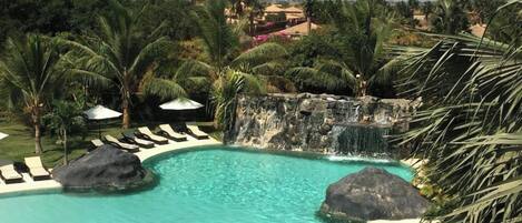 A clear blue pool with lounge chairs and a waterfall feature.