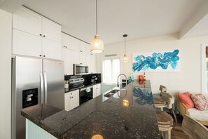 A modern kitchen with white cabinets, stainless steel appliances, a granite countertop, pendant lighting, and a large abstract painting. - Beach Therapy Your Historic Florida Cottage Escape in Key West (Key West, FL 33040)