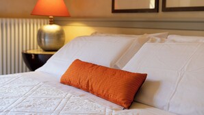 Een net opgemaakt bed met een gebogen hoofdbord, één oranje kussen en een bedlampje op een nachtkastje.