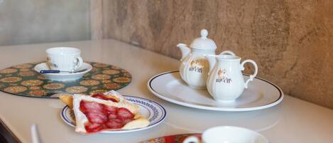 A table with a teapot, cups, saucers, and a slice of strawberry shortcake.