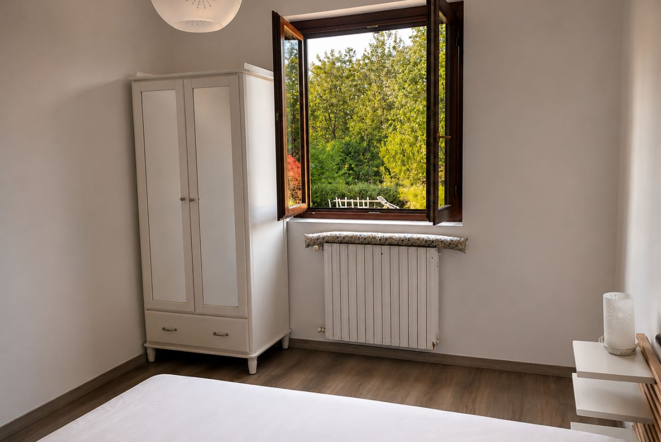 Ein Schlafzimmer mit Fenster, Heizkörper, Kleiderschrank und Nachttisch.