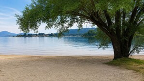 Vista de un lago bordeado de árboles, con una playa de arena y aguas tranquilas.