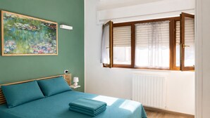 Un dormitorio con una cama, una ventana con persianas, un radiador y un cuadro en la pared.