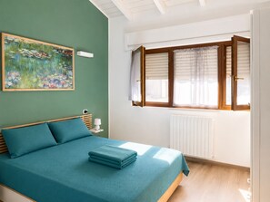 A bedroom with a bed, a window with blinds, a radiator, and a painting on the wall. - Cozy Villa Near Lake Maggiore and Malpensa Airport (Villaggi)