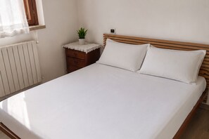 Ein Einzelzimmer mit einem hölzernen Kopfteil, einem Nachttisch mit Pflanze und einem weißen Heizkörper.
